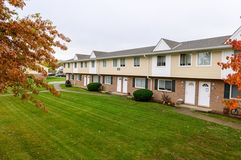 a row of townhomes with a green lawn and trees