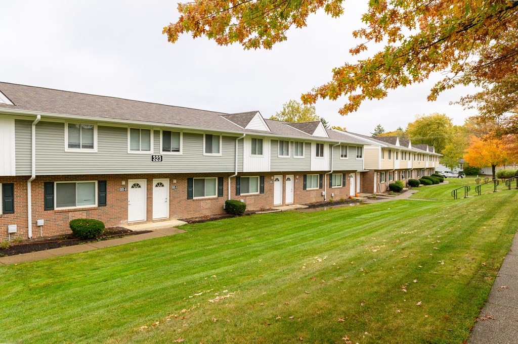 a row of condominiums on the side of a green lawn