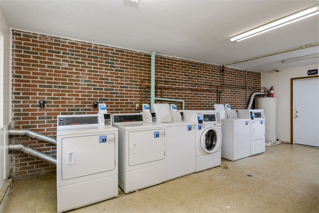 a laundry room with four washing machines and a brick wall