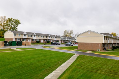 the view of an apartment complex with green grass and cars parked in front of it