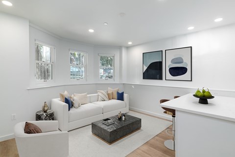 A white couch with pillows sits in a living room with a coffee table in front of it.