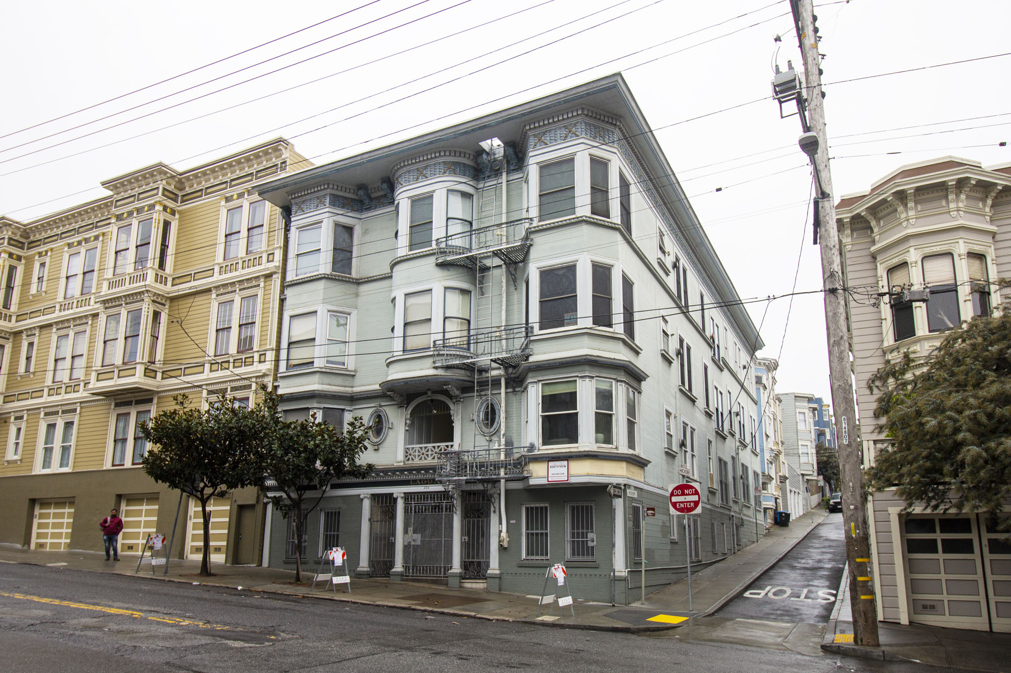 A street view of a row of Victorian style houses with a "No Stopping" sign on the sidewalk.
