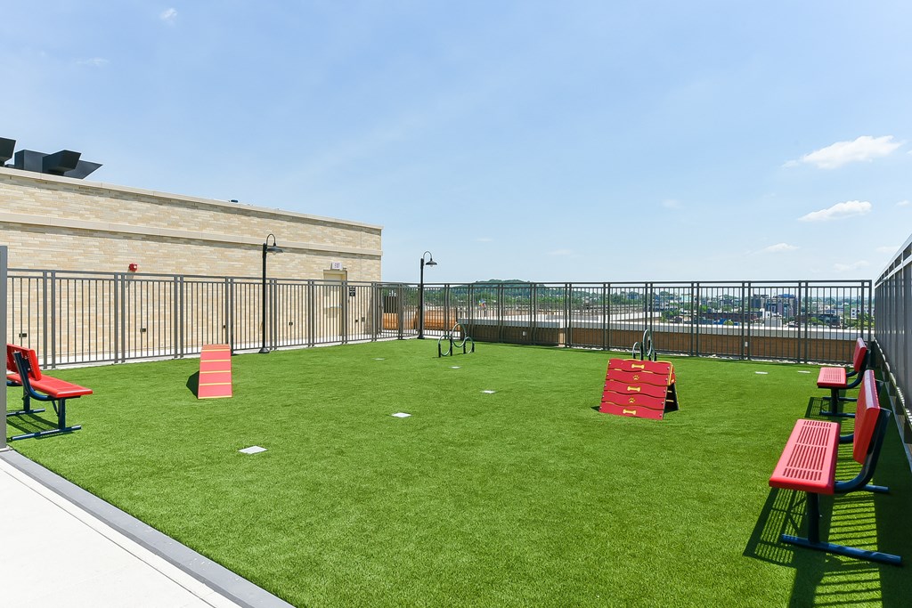 a rooftop grassy area with red chairs and a fence