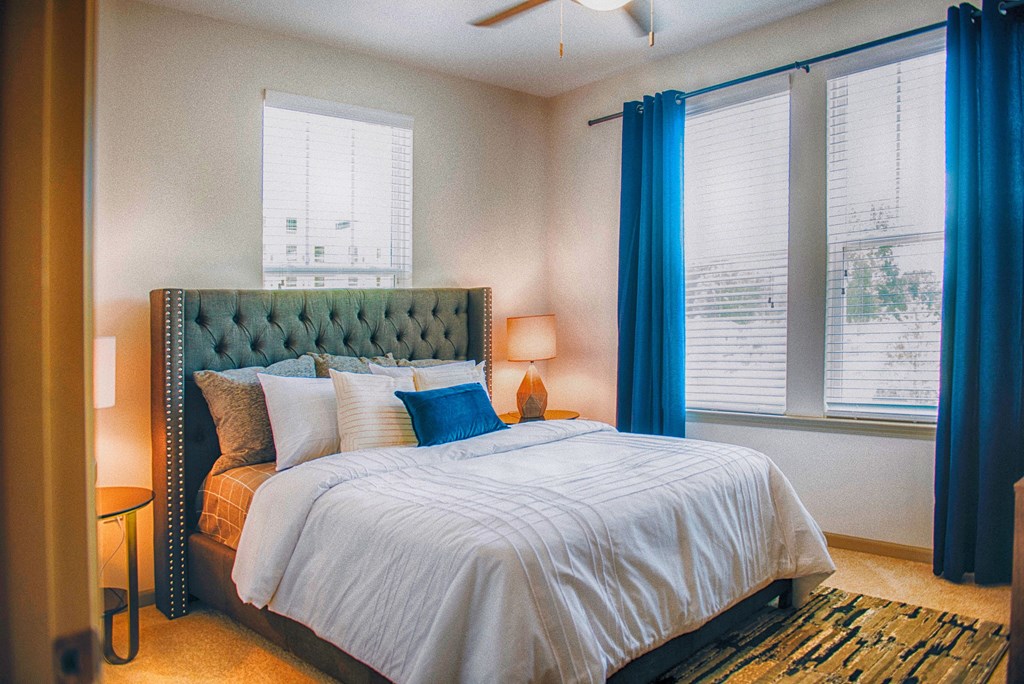 a bedroom with a bed and two windows with blue curtains