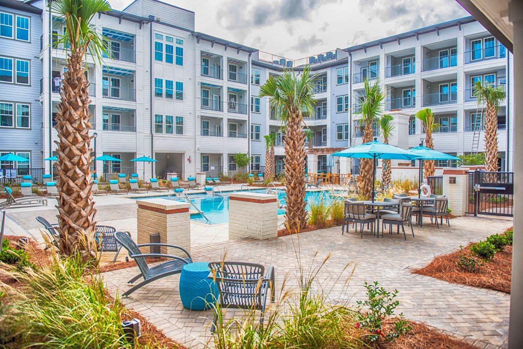 an outdoor pool with tables and umbrellas in front of an apartment building