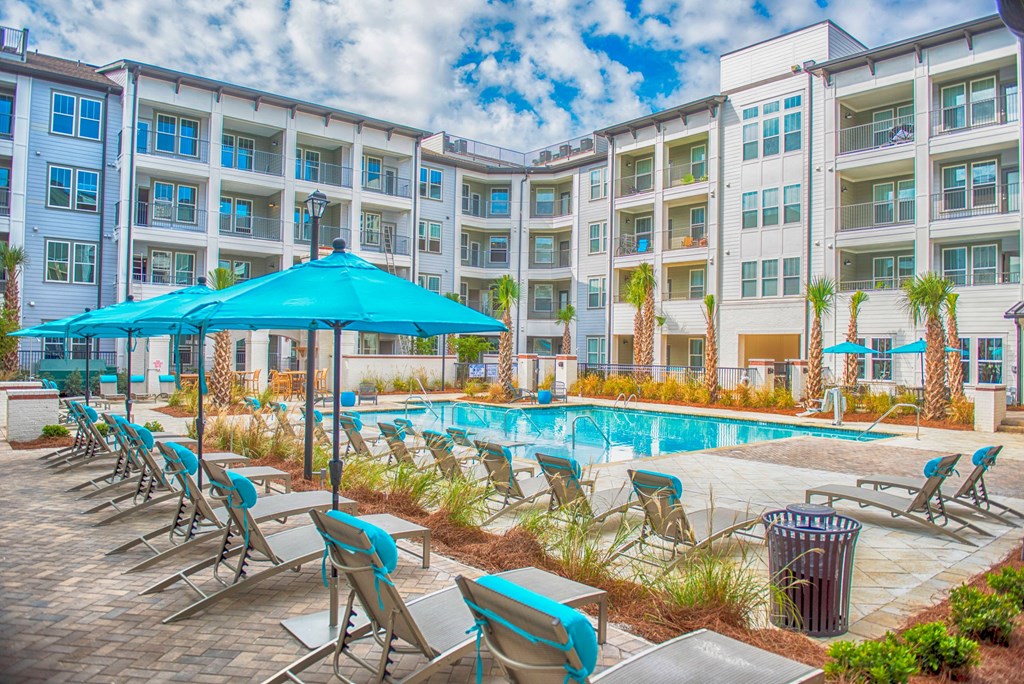 a swimming pool with chairs and umbrellas in front of an apartment building