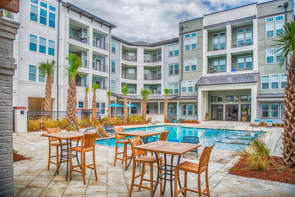 a patio with tables and chairs around a swimming pool in front of an apartment building