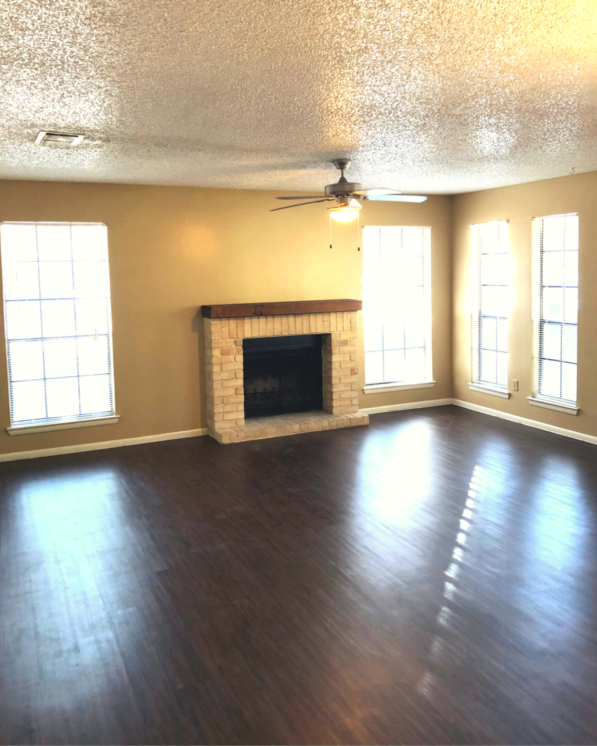 open living room with dark hardwood floors, a fireplace, and 4 wall length windows