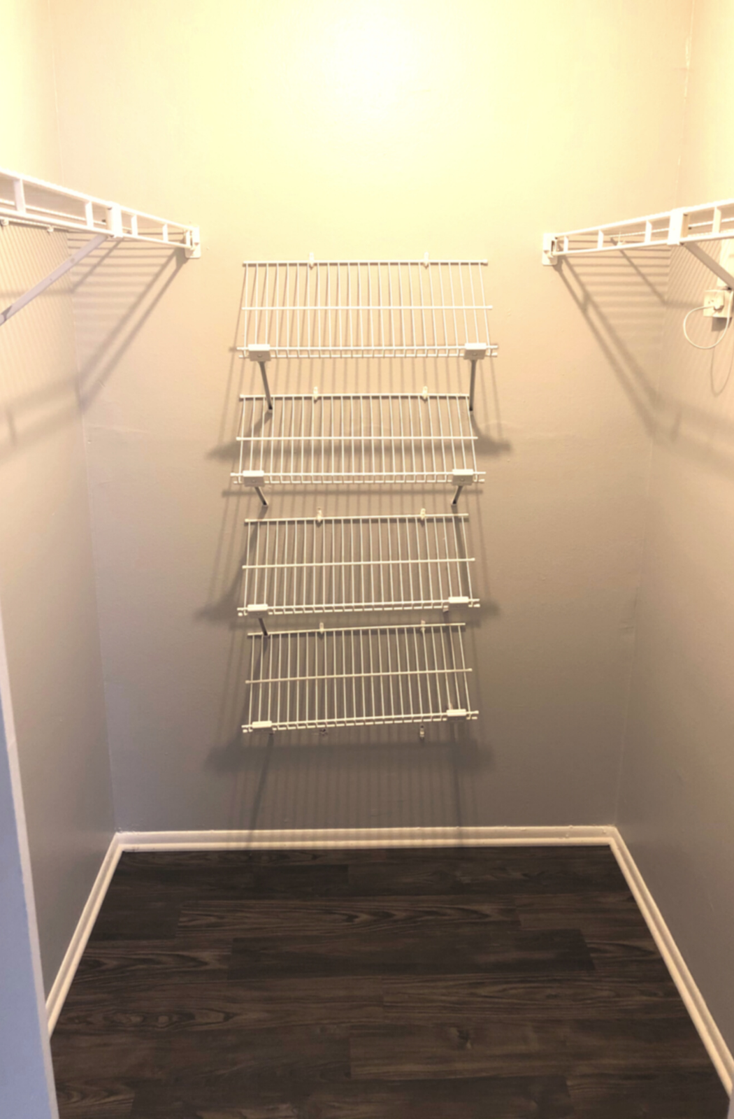 bedroom closet with dark wood floors, light grey walls and shoe racks