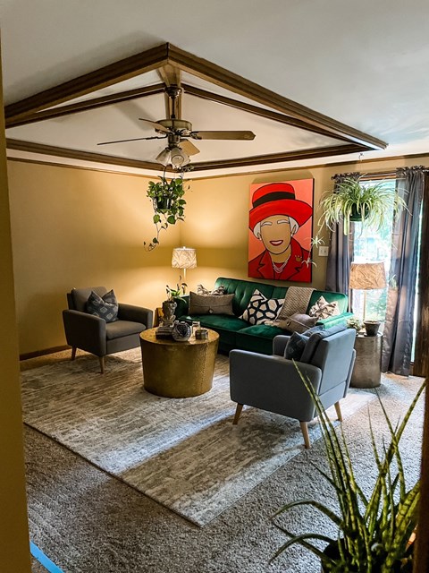A living room with a grey couch, a green couch, a coffee table, a ceiling fan, and a painting of a woman wearing a red hat.