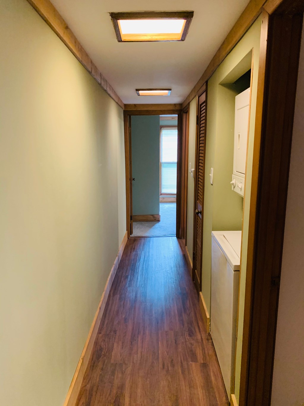 a long hallway with wood floors and a door to a bathroom