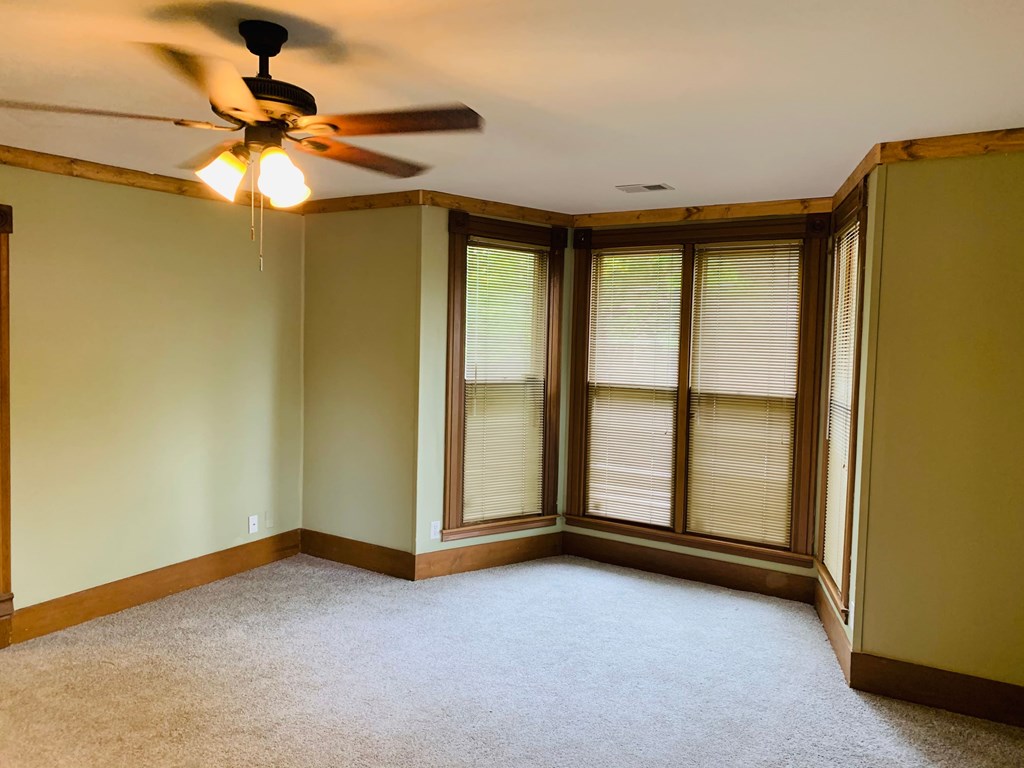 an empty living room with a ceiling fan and windows