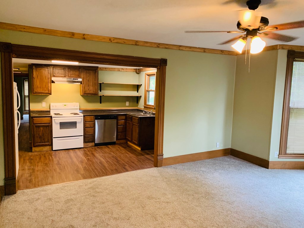 an empty living room with a kitchen and a ceiling fan