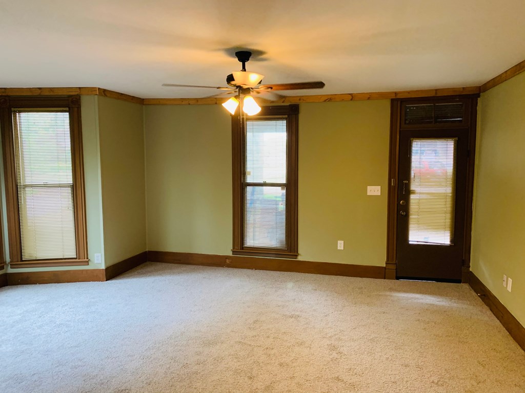 an empty living room with a ceiling fan and windows