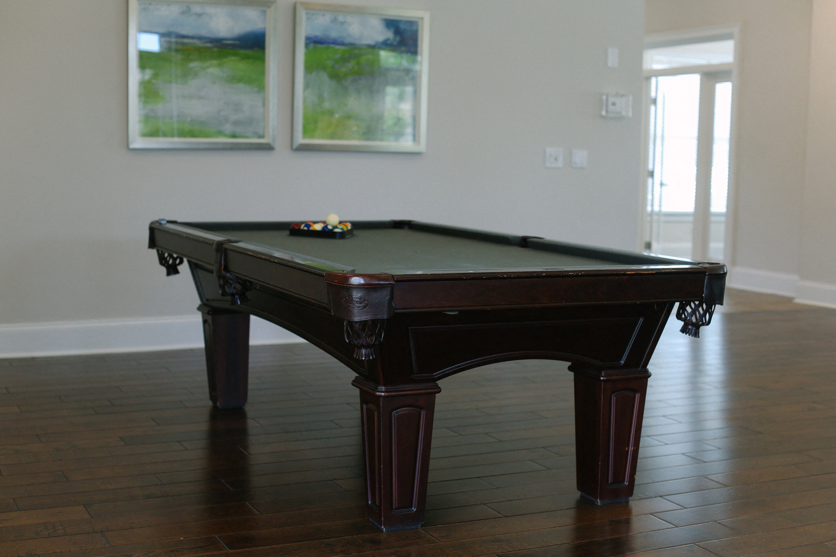 a pool table in a living room with two paintings on the wall