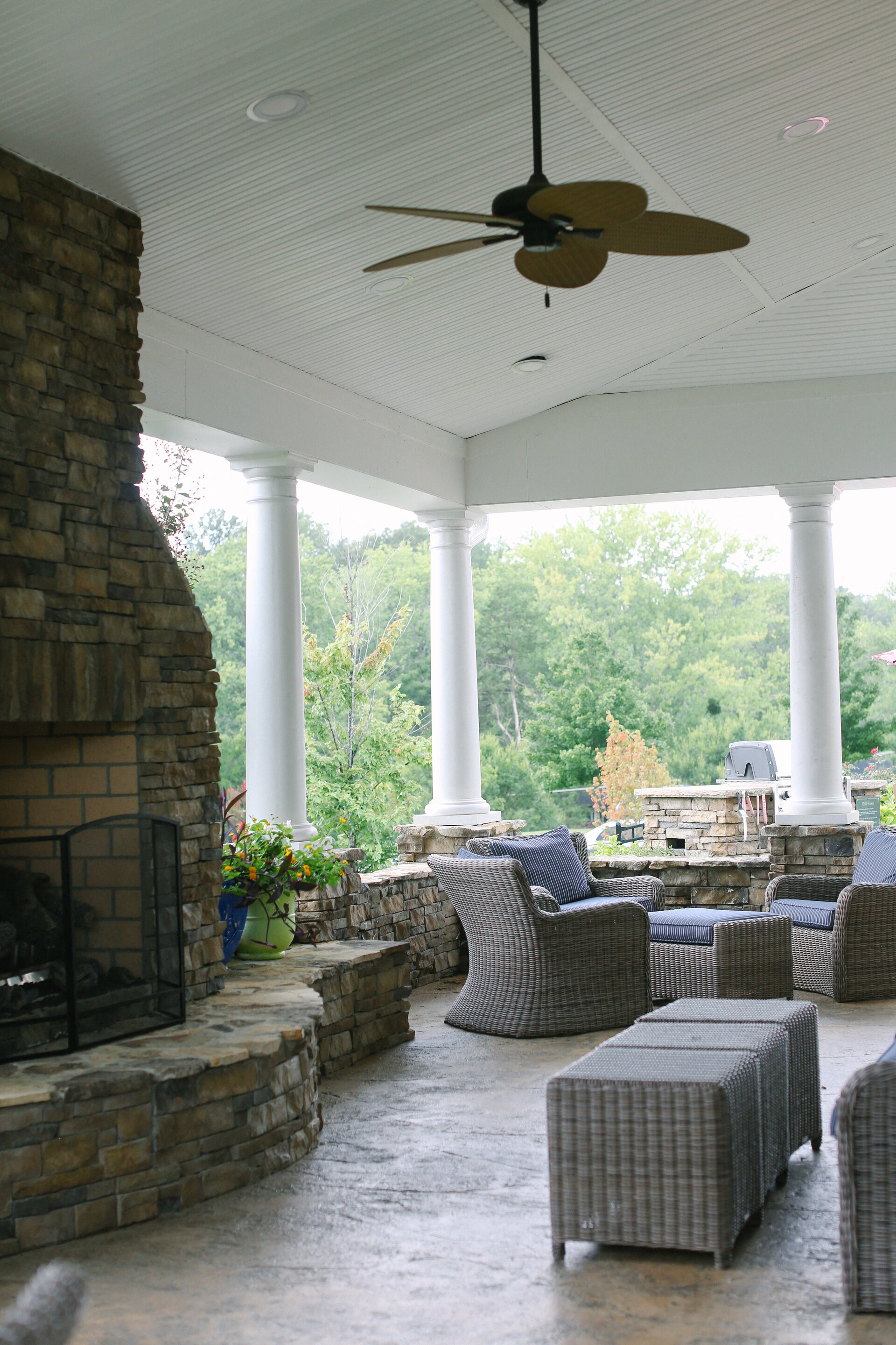 a screened in porch with a stone fireplace and a ceiling fan