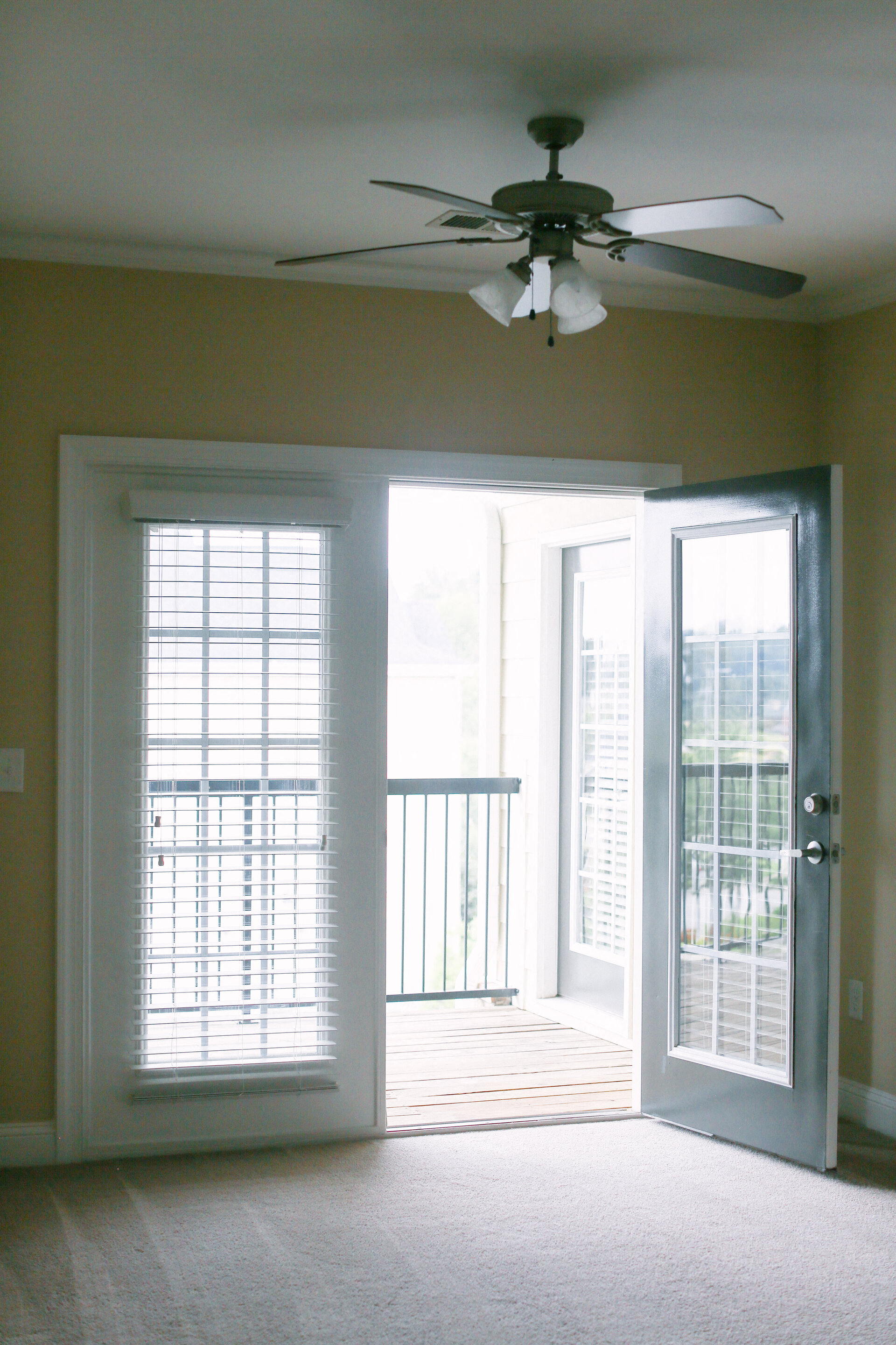an empty living room with a ceiling fan and a balcony