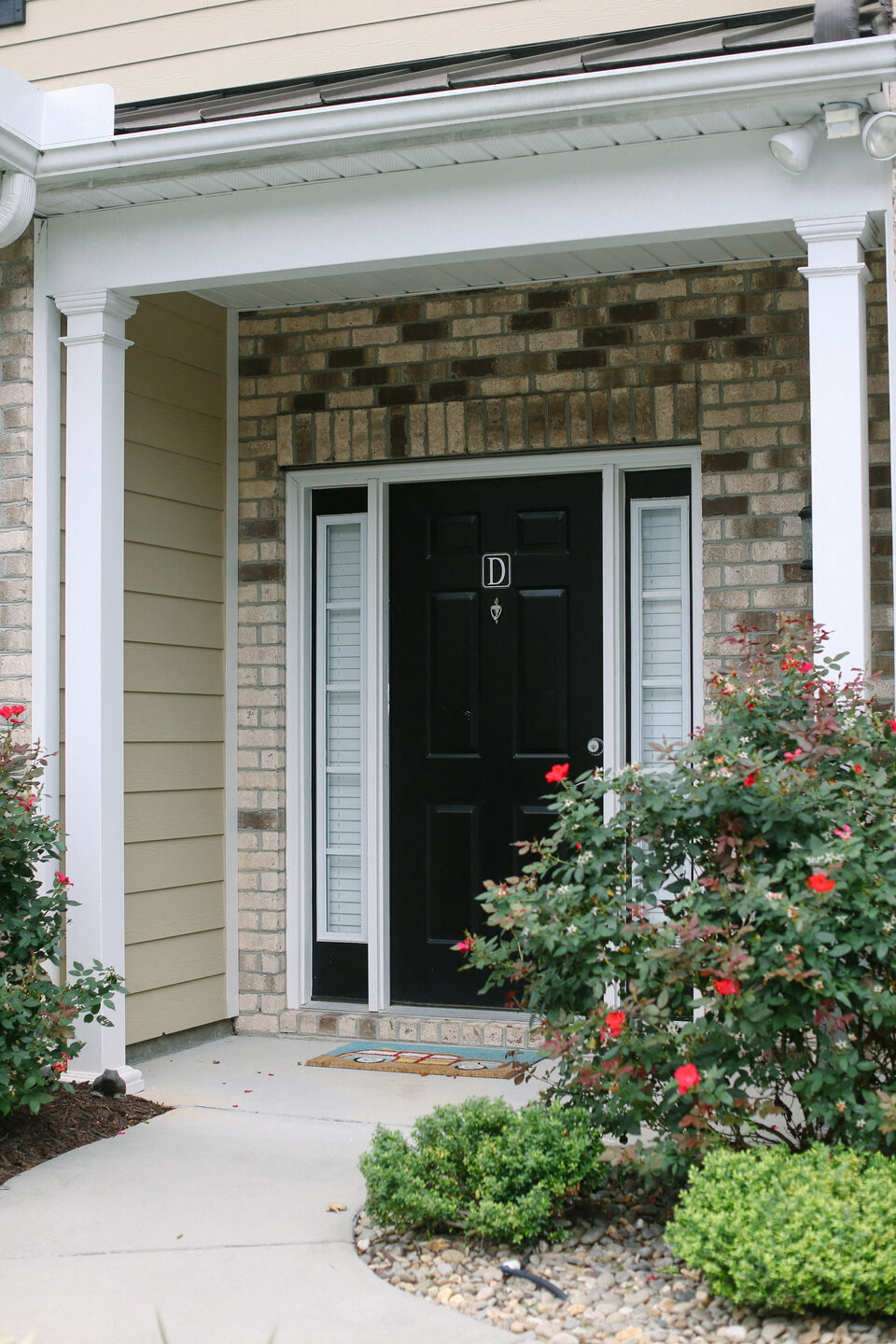 the front door of a house with a black door and a porch with red flowers