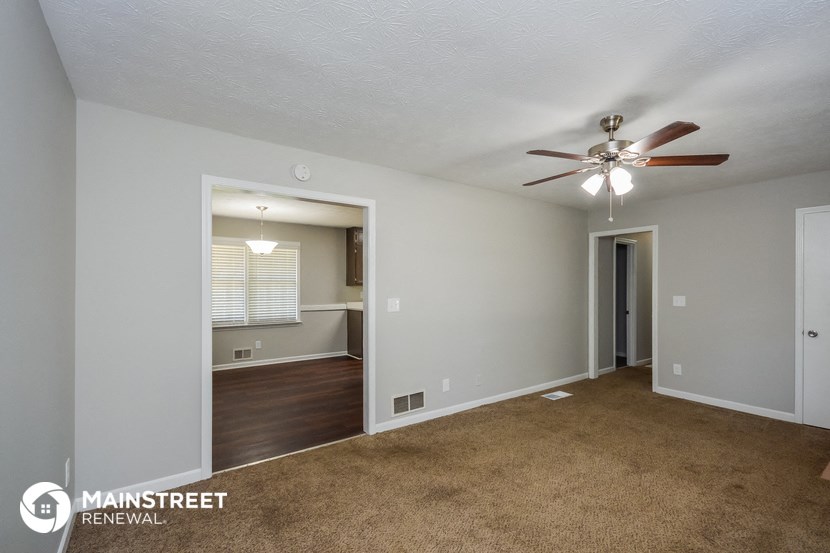an empty living room with a ceiling fan and a door to a kitchen