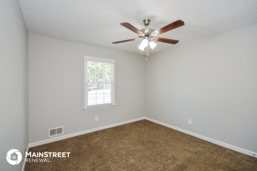 the spacious living room has carpet and a ceiling fan
