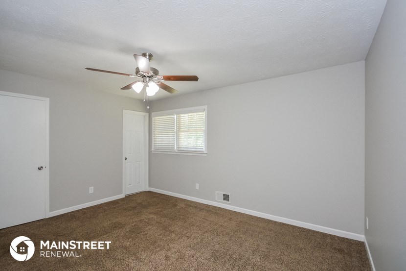the spacious living room with ceiling fan and carpet