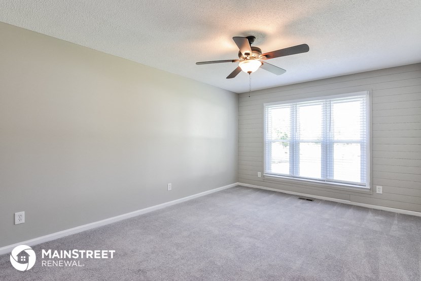 the spacious living room with ceiling fan and window