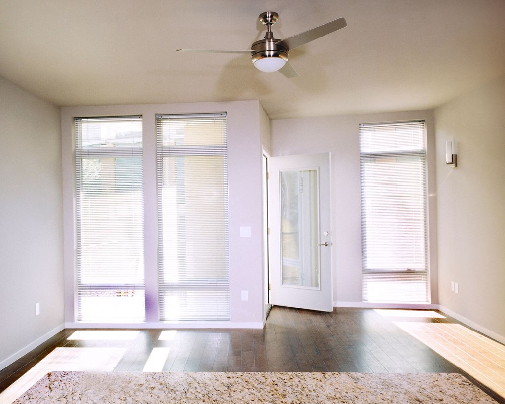 an empty living room with a ceiling fan and windows