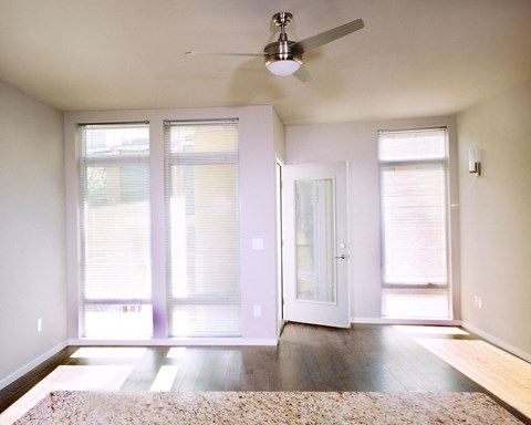 an empty living room with a ceiling fan and windows