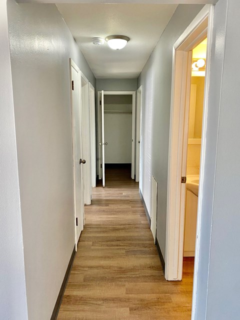 a hallway with a wood floor and white walls and a hall way to a bedroom
