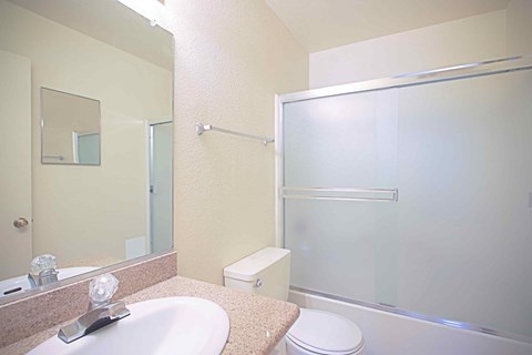A bathroom with a toilet, sink, mirror, and shower.
