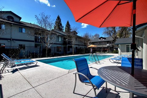 A pool area with a table and chairs and an umbrella.