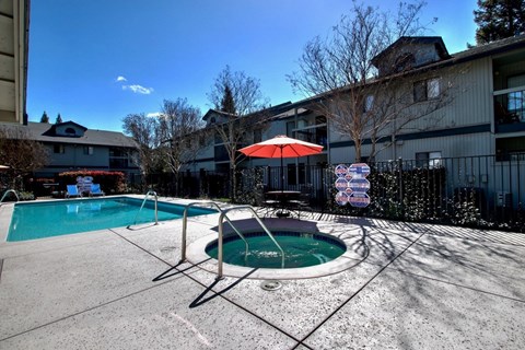 A swimming pool with a red umbrella and a sign in the background.