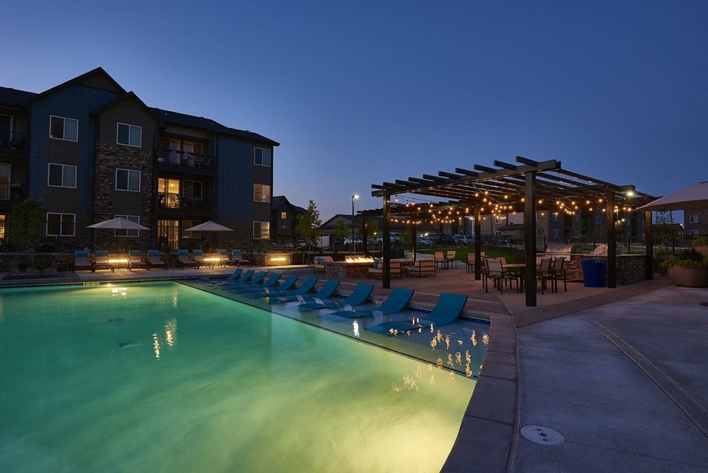a swimming pool at night with lounge chairs and umbrellas