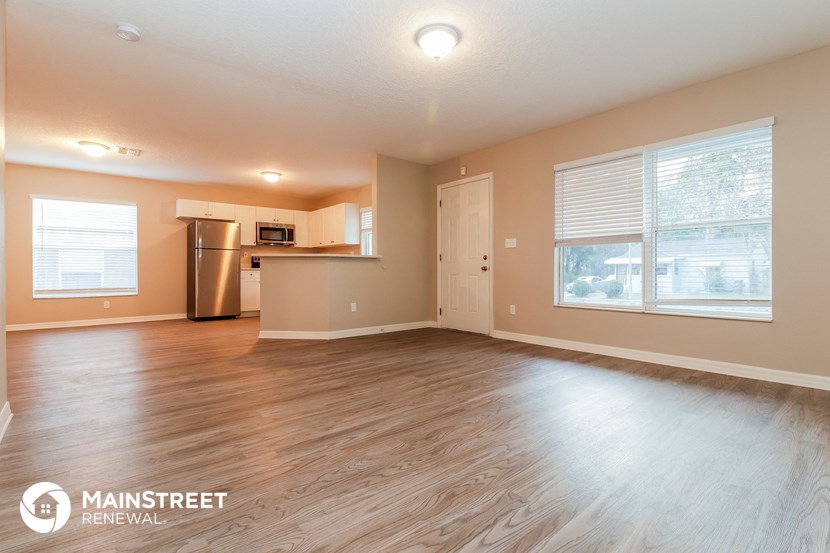 an empty living room with a kitchen and a large window