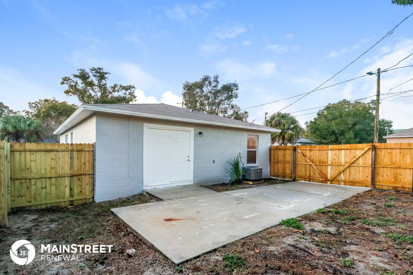 the backyard of a small white house with a wooden fence