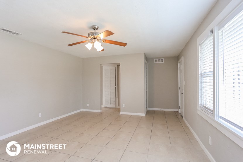 an empty living room with a ceiling fan and large windows