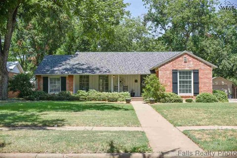 A house with a brick facade and a grey roof is surrounded by greenery.
