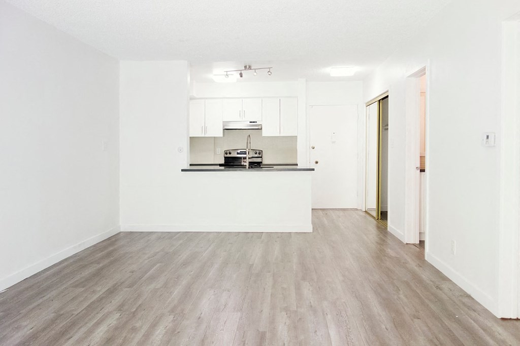 an empty living room and kitchen with white walls and wood floors