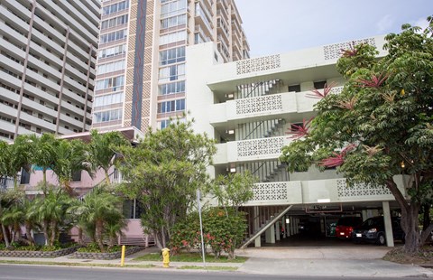 A white building with a red roof is in front of a taller building.