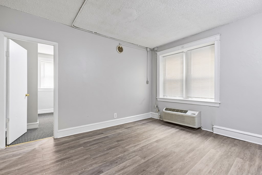 an empty living room with white walls and wood flooring and an air conditioner