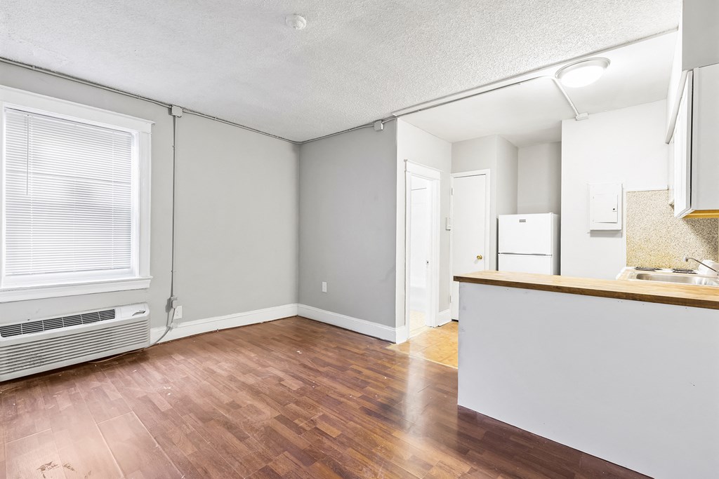 the living room and kitchen of an apartment with hardwood flooring and a window