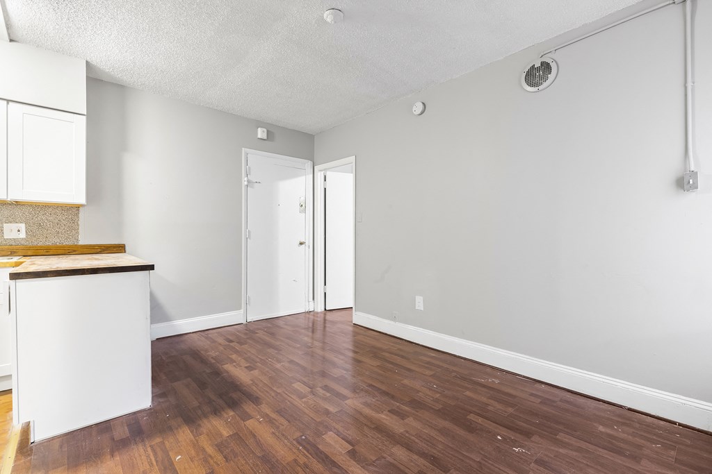 an empty living room and kitchen with wood floors and white walls
