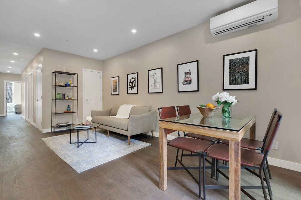 A modern living room with a glass table and chairs, a sofa, and framed pictures on the wall.