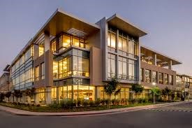A modern building with large windows and balconies is illuminated at dusk.