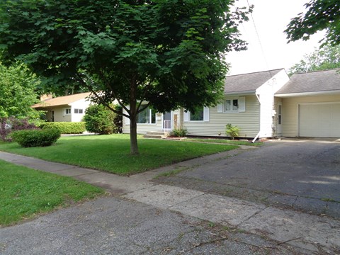 a white house on a street with a sidewalk and trees