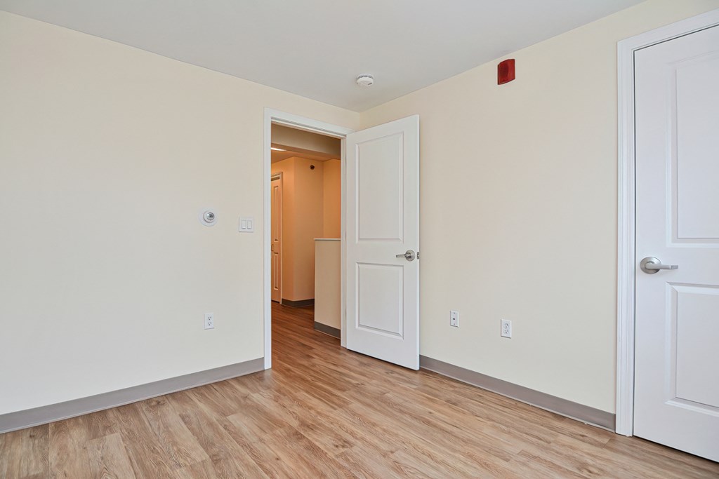 a bedroom with white walls and wood flooring and a door to a closet
