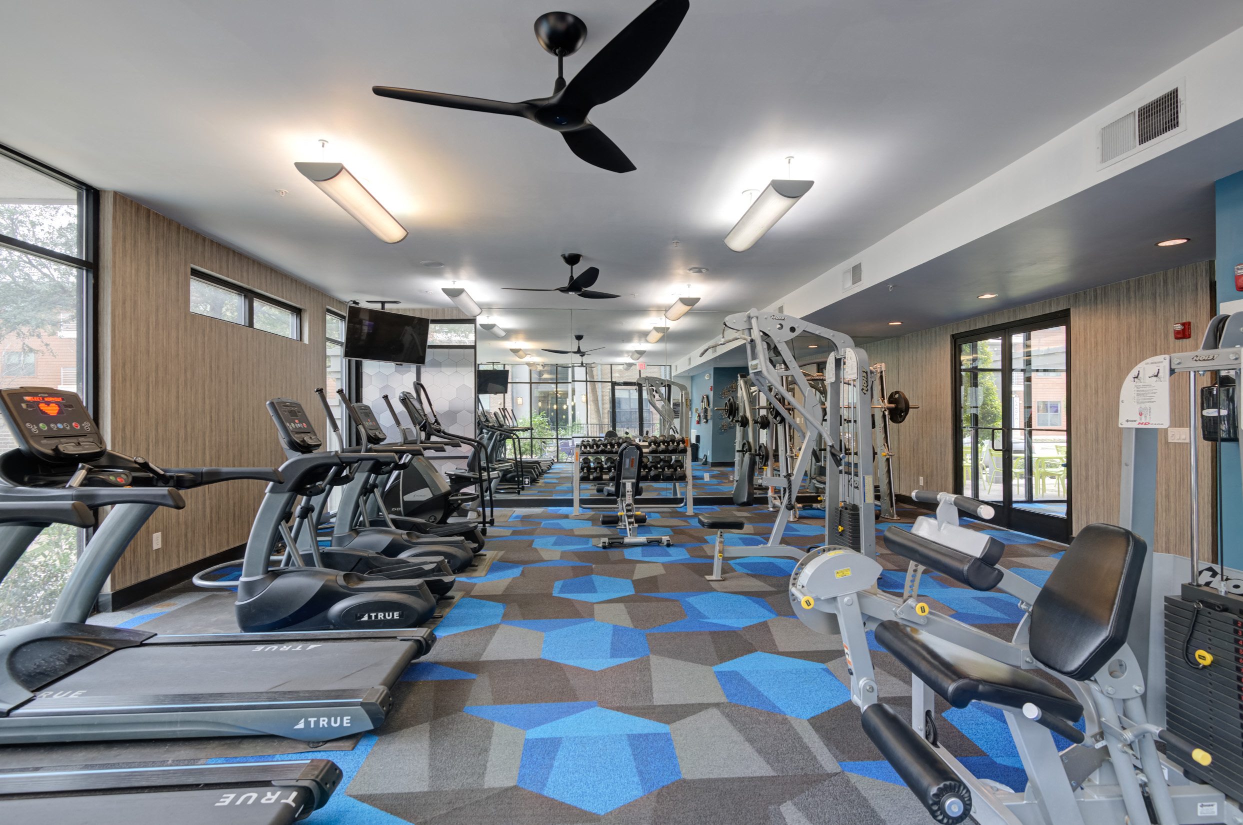 a gym with cardio equipment and a ceiling fan