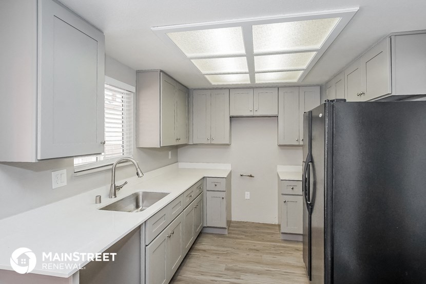 a kitchen with white counters and white cabinets and a black refrigerator