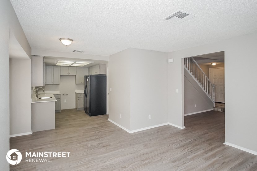 the living room and kitchen of an apartment with white walls and wood flooring