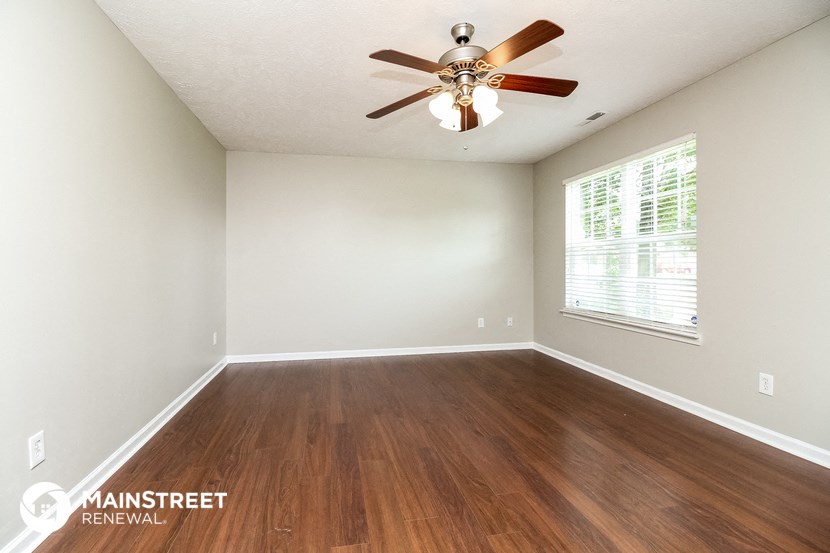the spacious living room with hardwood flooring and a ceiling fan